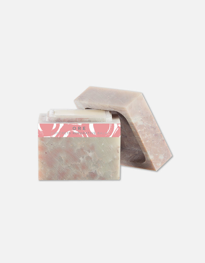 Two bars of natural soap with a soft earthy tone and a pink label, next to a clear lip balm, representing Concreta | Zents skincare products.