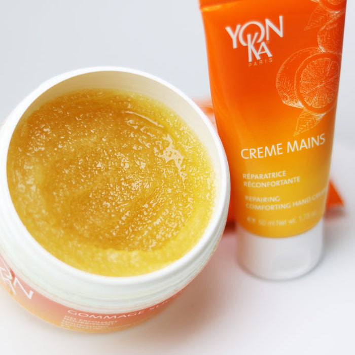 Open container of golden sugar body scrub next to an orange tube of hand cream, showcasing skincare products for body care and wellness featuring Gommage Sucre Mandarin Body Scrub | Yon-Ka Paris.