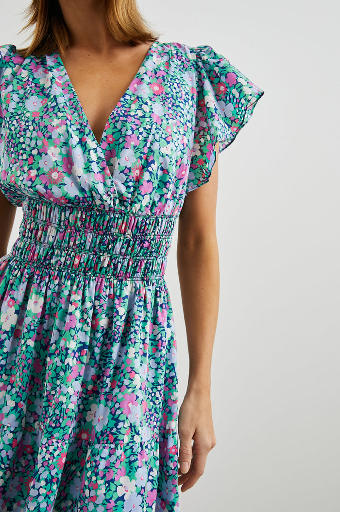 Kimora Above-Knee Dress with Flutter Sleeves, a V Neckline, a Cinched Waist and a Tiered Skirt in Navy Leilani Floral Colorway with flowers in pinks, purples and greens - Front View Featured on Model