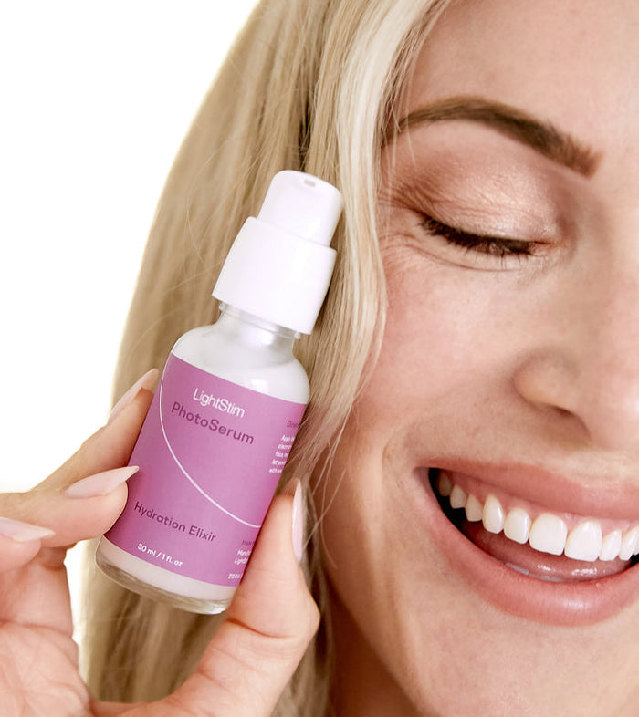 A smiling woman holding a bottle of LightStim PhotoSerum | LightStim with a lavender label, promoting skincare hydration and wellness.