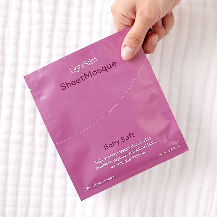A hand holding a pink packet of LightStim SheetMasque | LightStim Baby Soft, a skincare sheet mask designed to hydrate and nourish skin for a soft, glowing look.