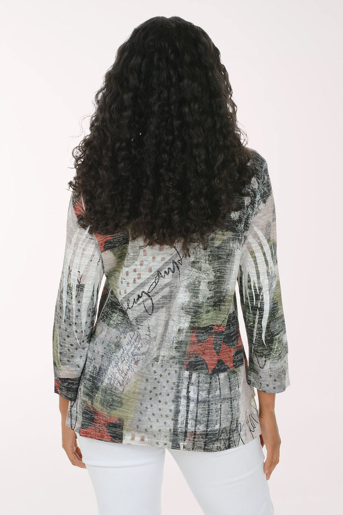 A woman with long, curly black hair is smiling and wearing a three-quarter sleeve top with an abstract, painterly print in gray, green, black, and red, paired with white pants, against a plain white studio background.